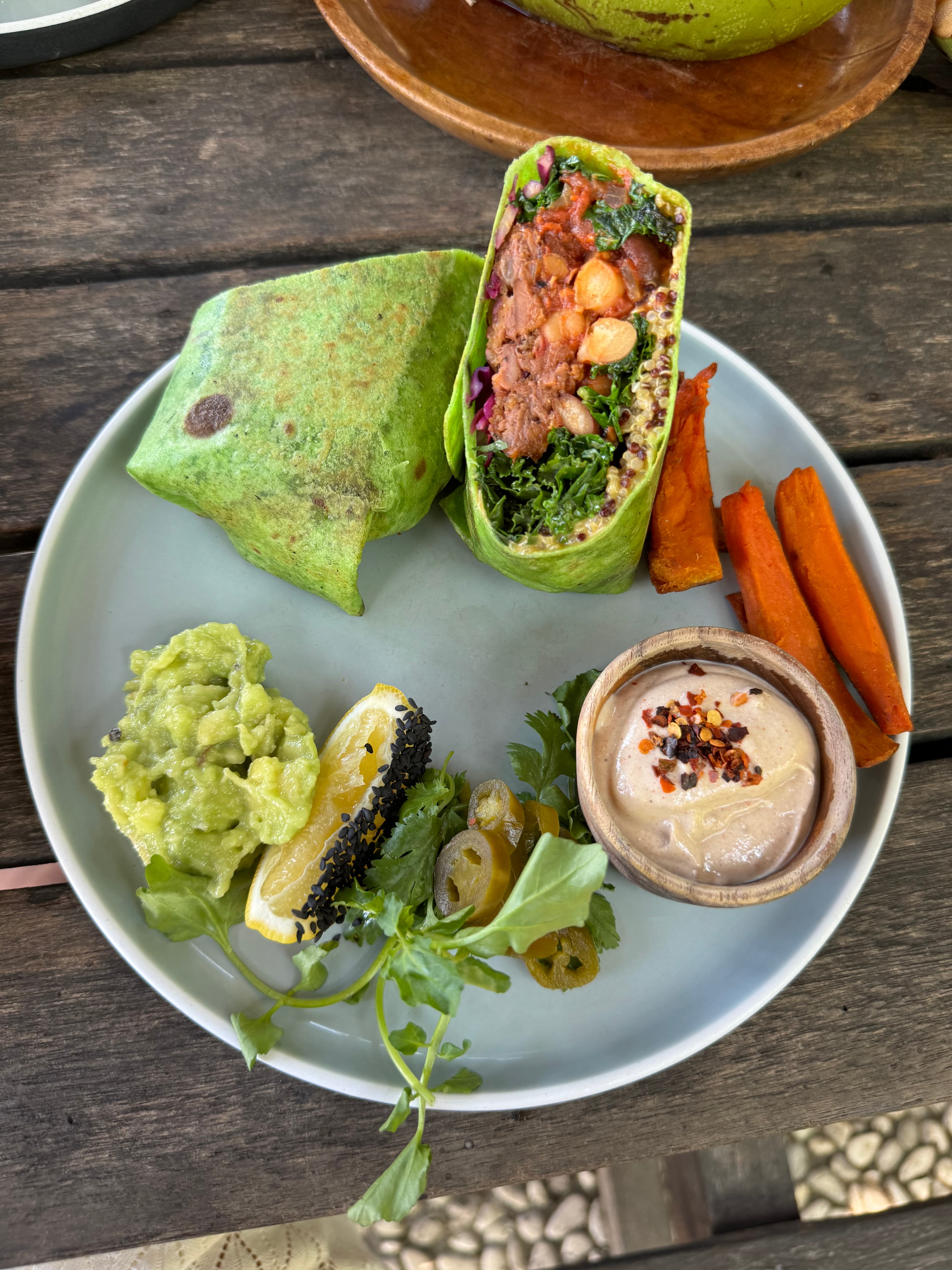 Green wrap with guacamole, sweet potato, and herbs on a wooden table