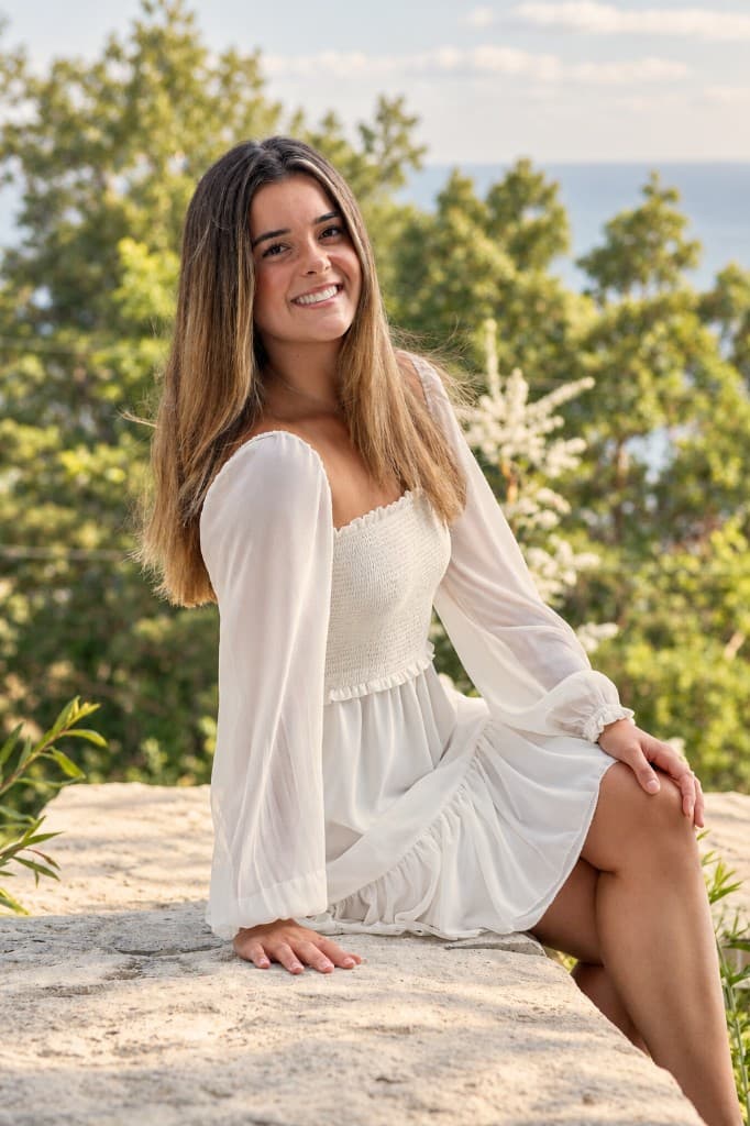 Jaz smiling outdoors in a white dress by the water