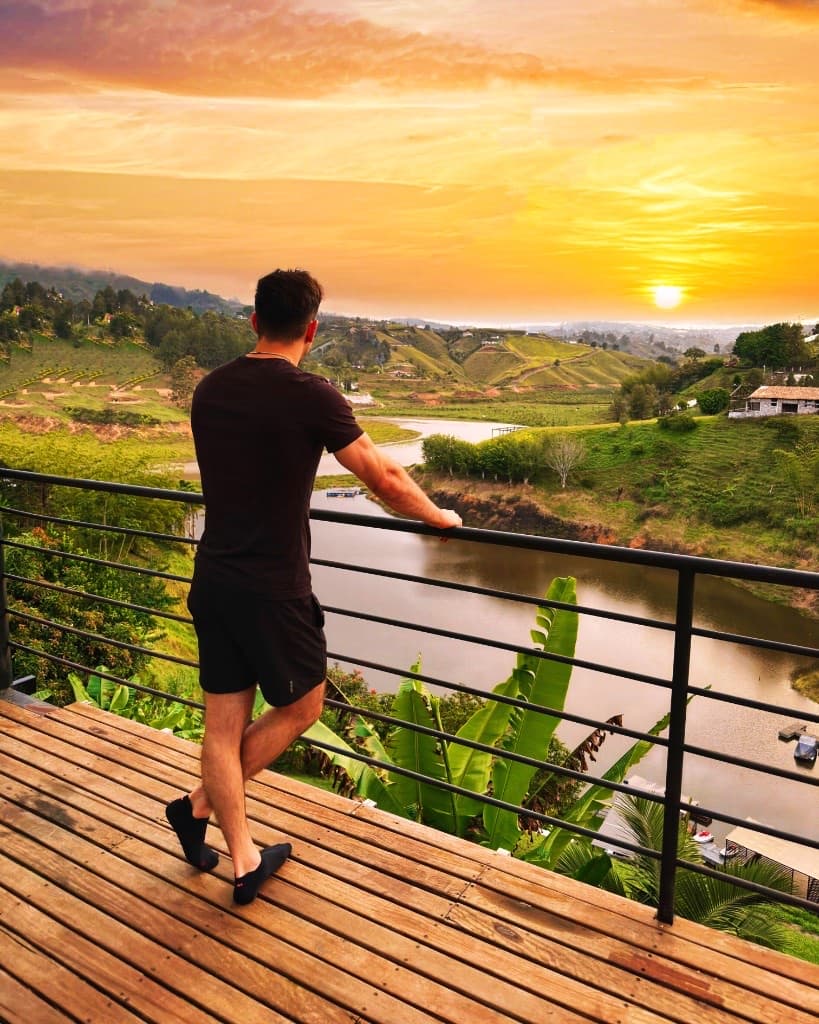 Michael at a railing overlooking green hills and water at sunset