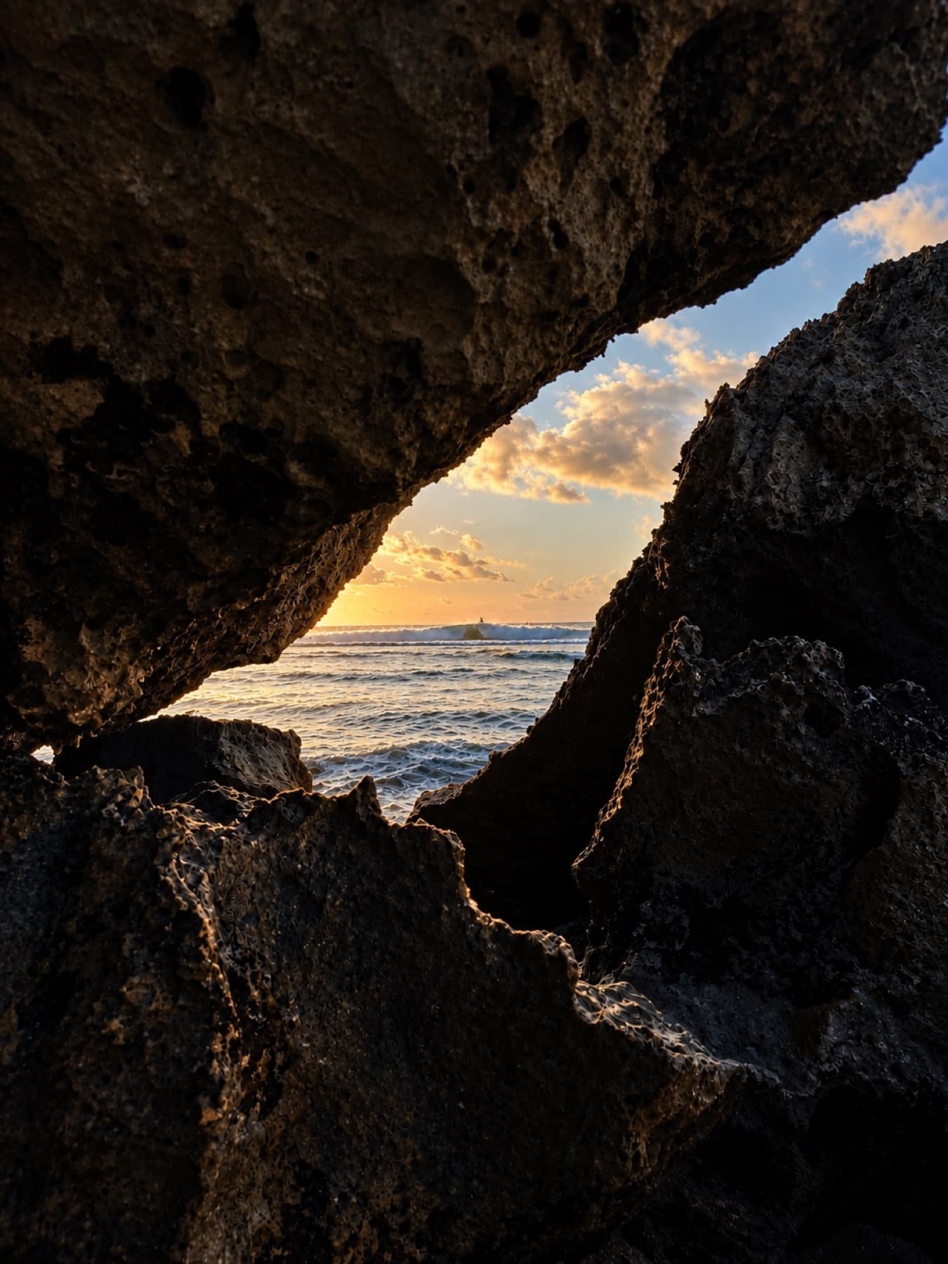 Ocean and golden sunset framed by a dark rocky cave opening