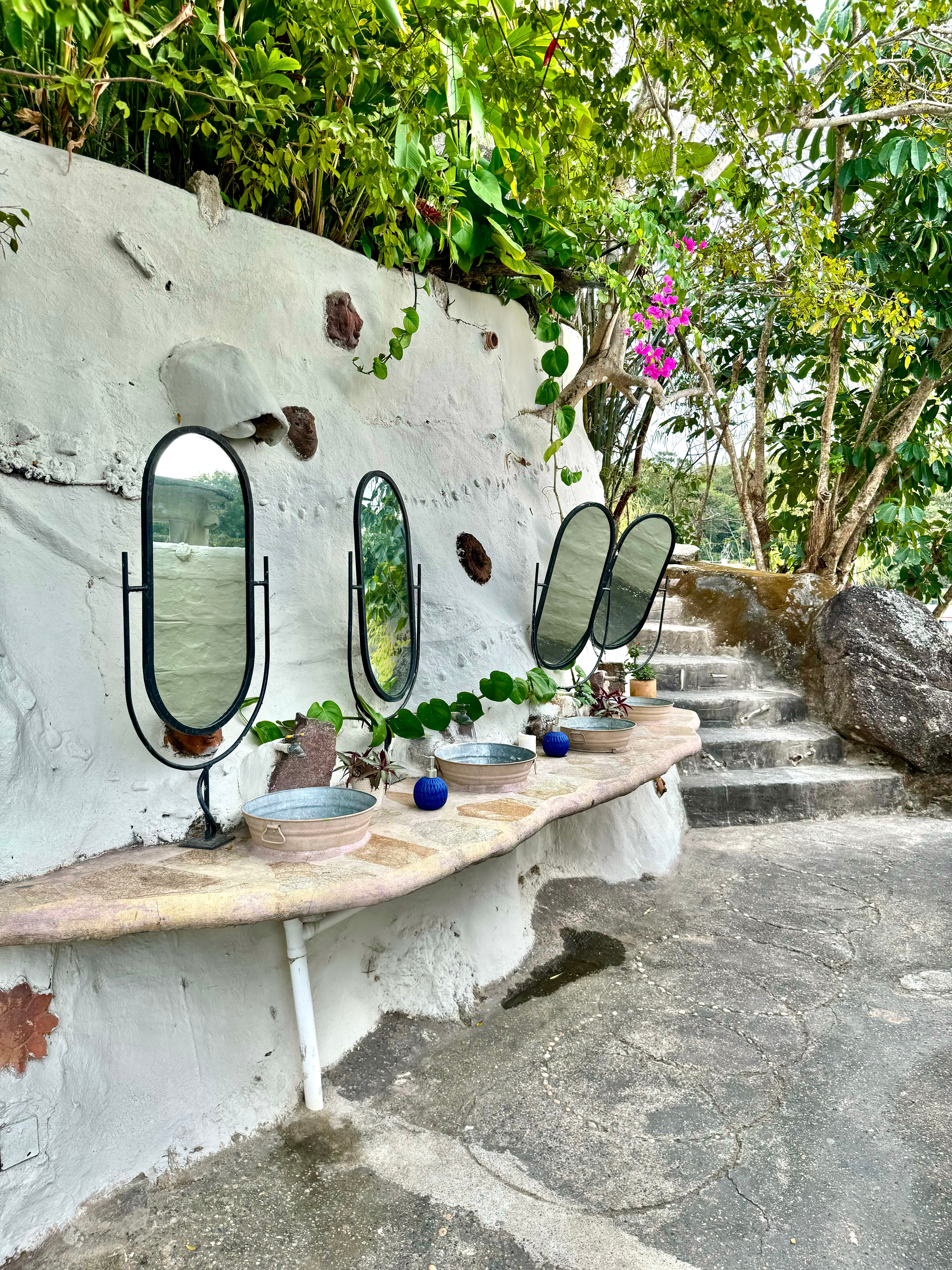 Rustic outdoor sink row with mirrors set into tropical greenery